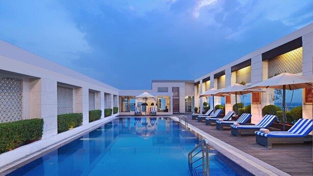 A modern hotel pool area with a clear sky, lounge chairs, and umbrellas. - Radisson Hotel Agra (Agra)