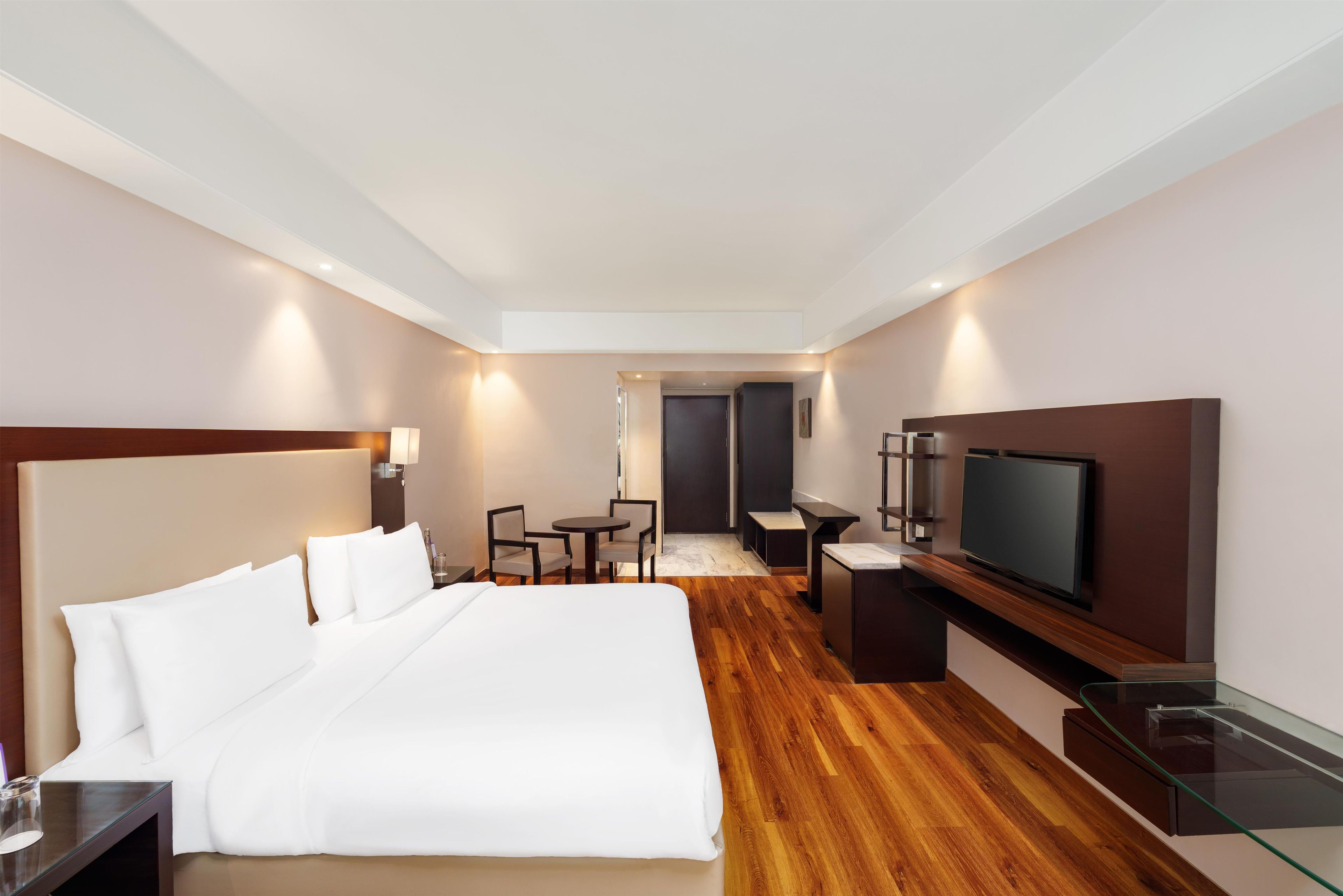 A hotel room with a large bed, a TV, a desk, and a chair.