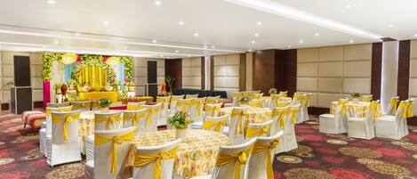 Une salle de banquet avec des tables rondes, des chaises ornées de rubans jaunes et une scène décorée de fleurs.