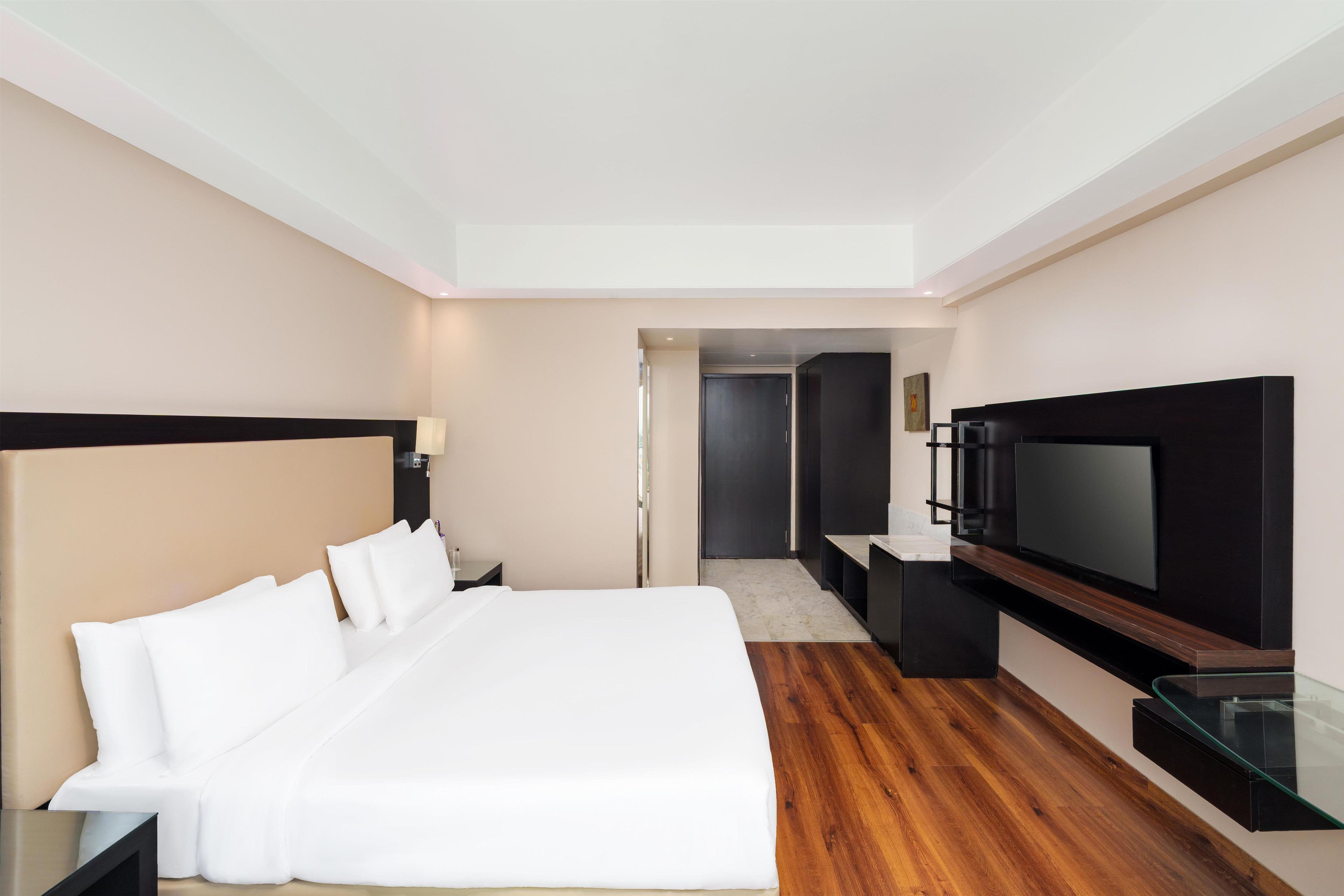 Quarto de hotel com uma cama grande, televisão de tela plana, piso de madeira e porta que dá para outro cômodo.