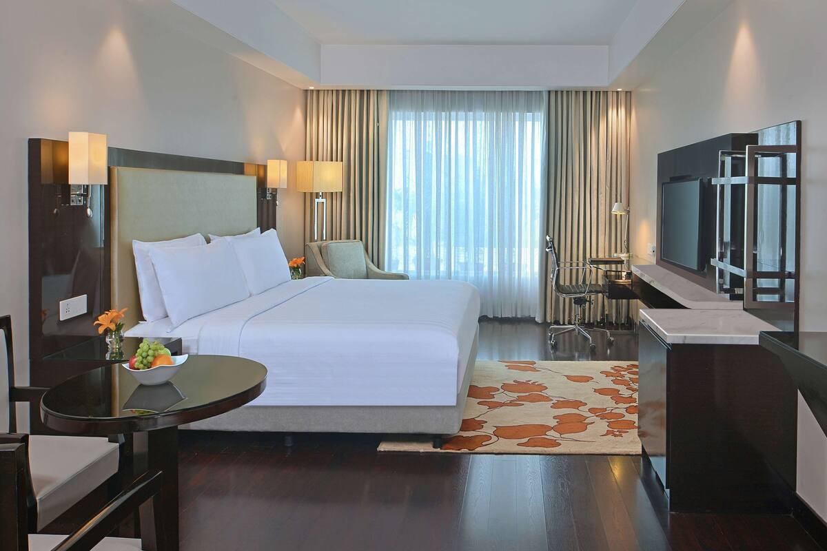 Una habitación de hotel con una cama grande, un escritorio con silla, un televisor y una ventana con cortinas.
