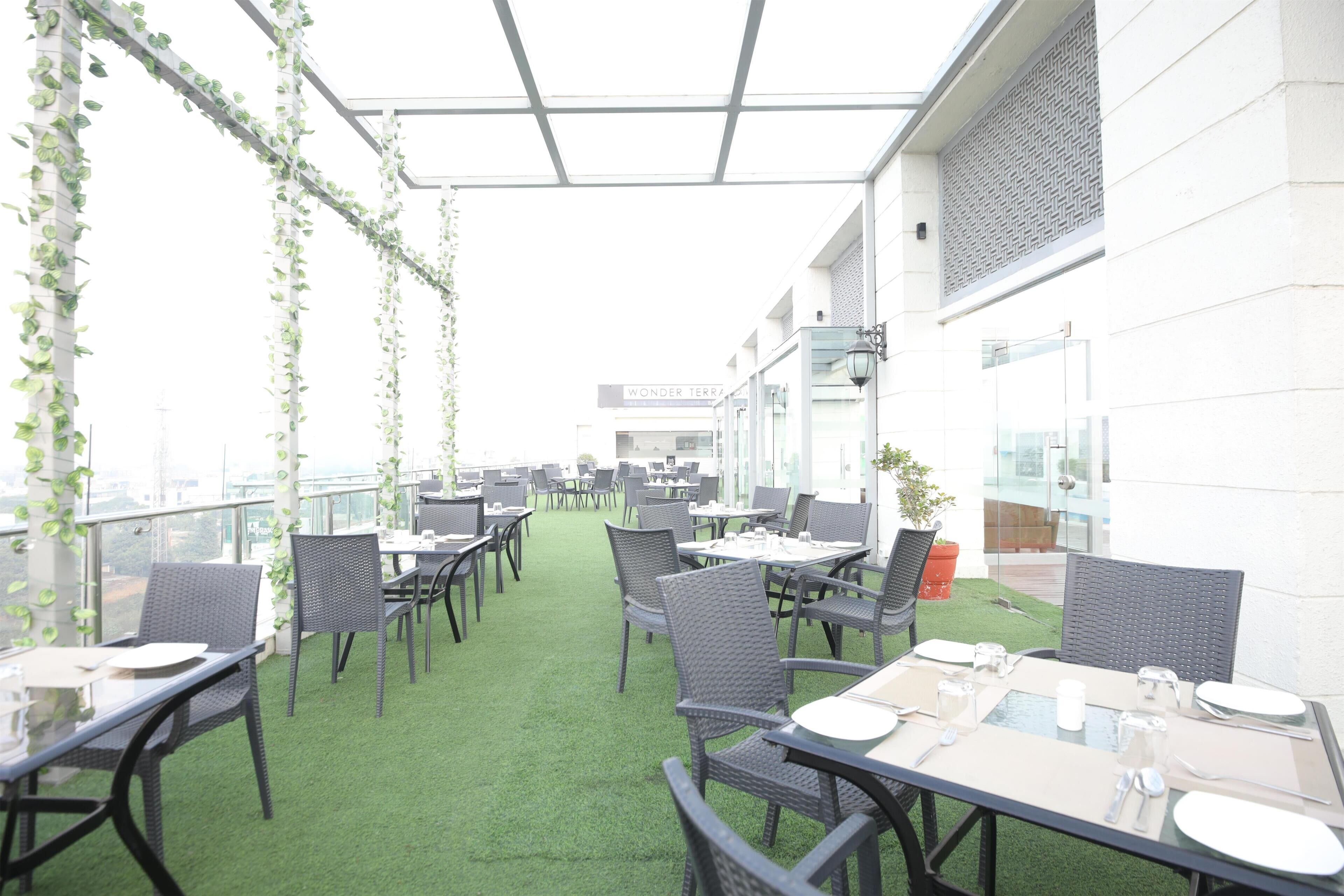 Un espace de restauration en plein air avec des tables et des chaises, un sol recouvert d’un gazon synthétique vert et une vue sur un bâtiment portant l’inscription « Wonder Terra ».
