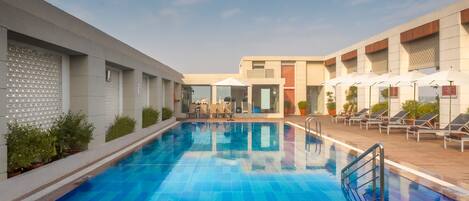 A swimming pool with a depth of 2.6 feet, surrounded by lounge chairs and umbrellas, with a modern building in the background.