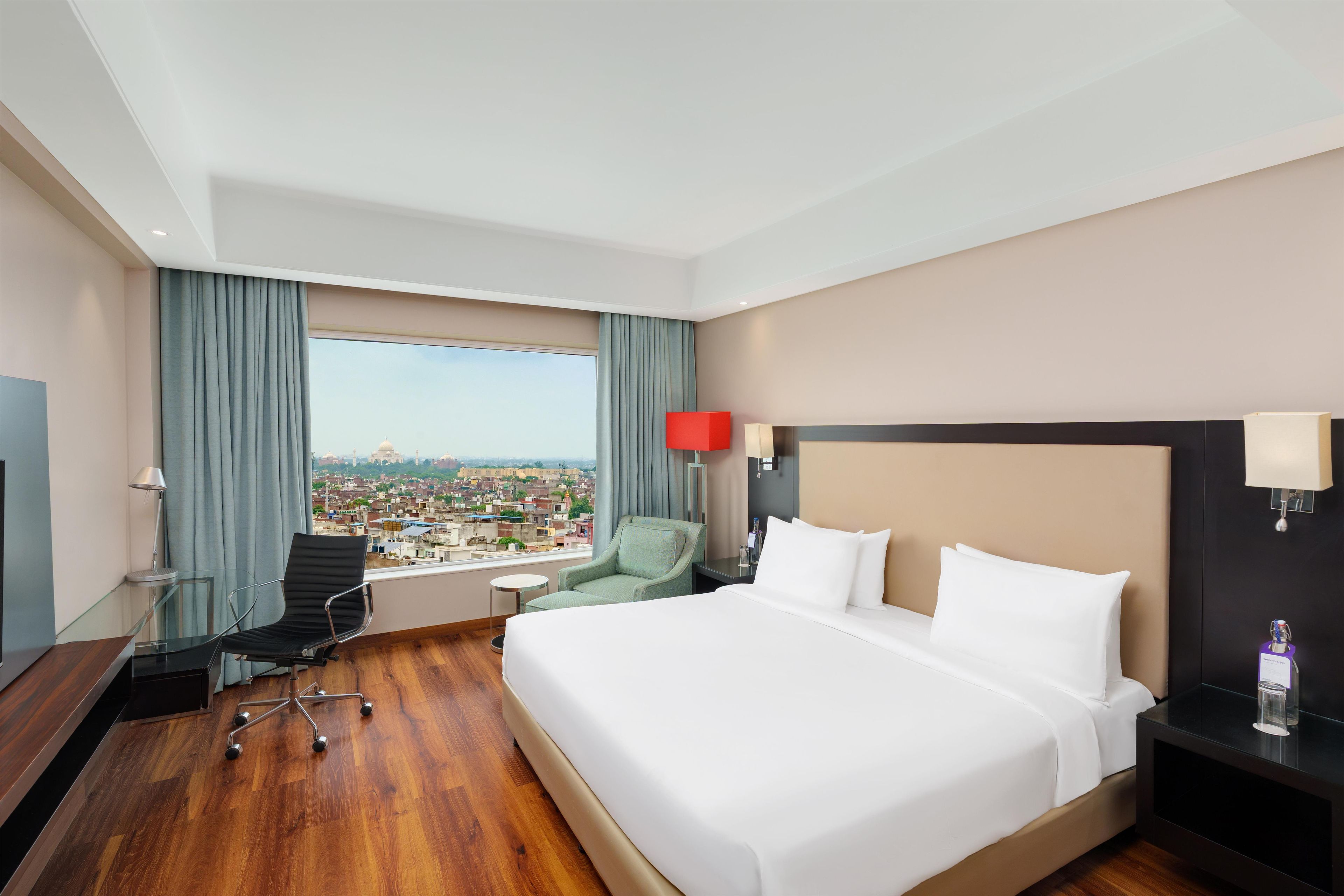 Ein Hotelzimmer mit einem großen Bett, einem Schreibtisch, einem Stuhl, einem kleinen Tisch und Blick auf die Stadt.