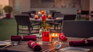 Una mesa de comedor dispuesta con un vaso de bebida roja, una rosa y una vela.