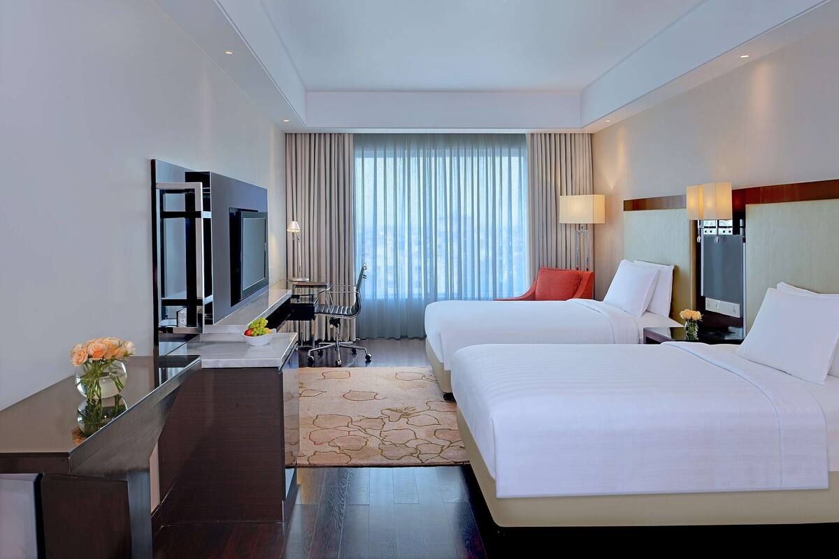 Habitación de hotel con dos camas, un escritorio, un televisor y una ventana con cortinas.
