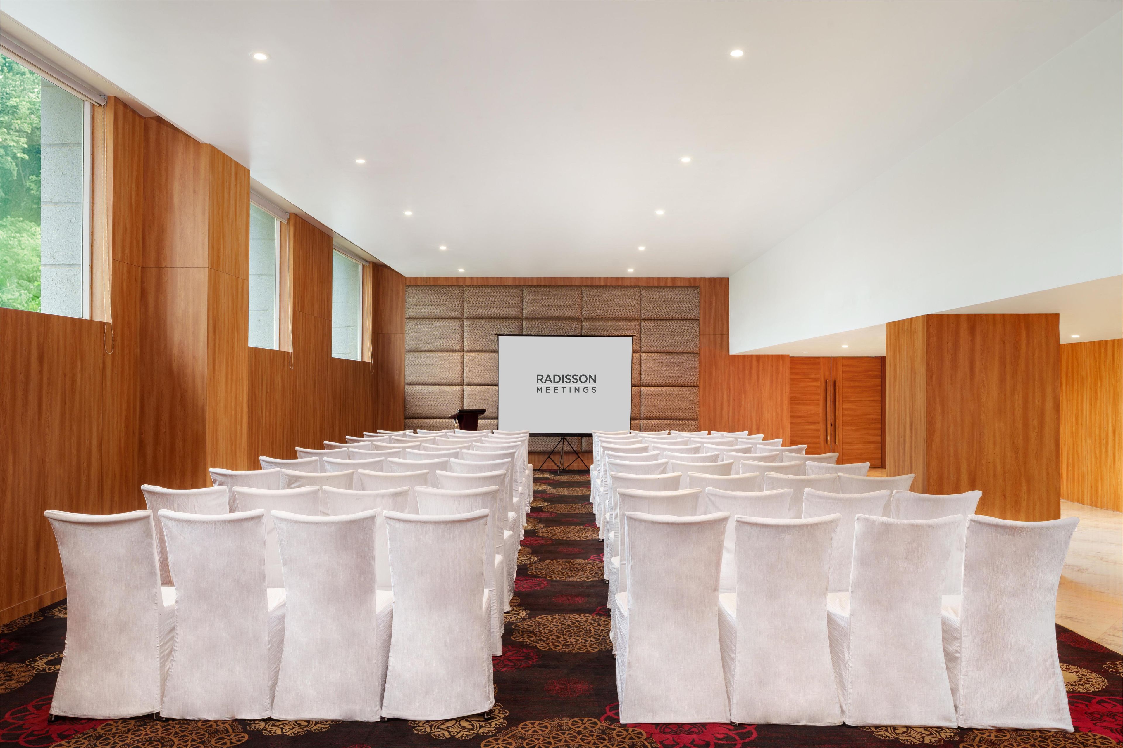 A conference room with rows of white chairs, a podium, and a projection screen for meetings.