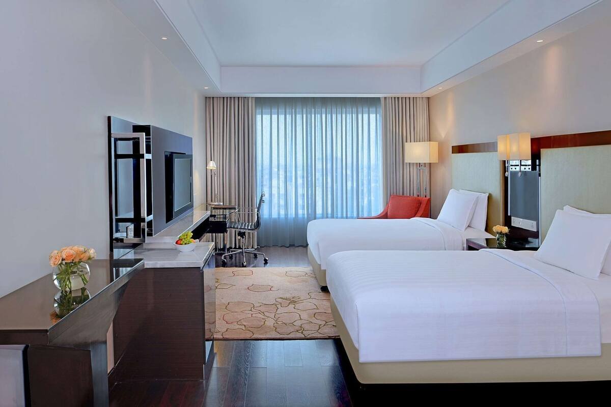 Una habitación de hotel con dos camas, un escritorio, un televisor y una ventana con cortinas.