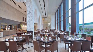 A spacious restaurant with high ceilings, large windows, and a modern interior design. - Radisson Hotel Agra (Agra)