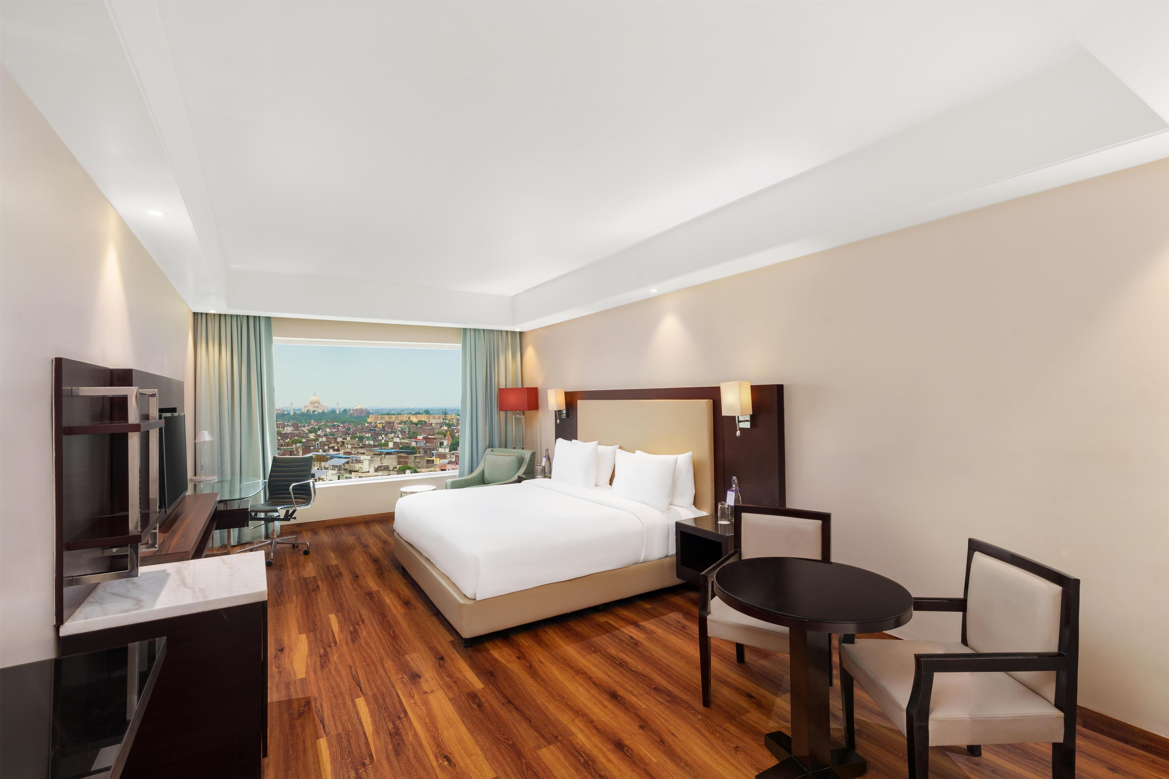 A hotel room with a bed, a desk, a chair, a table, and a view of a cityscape.