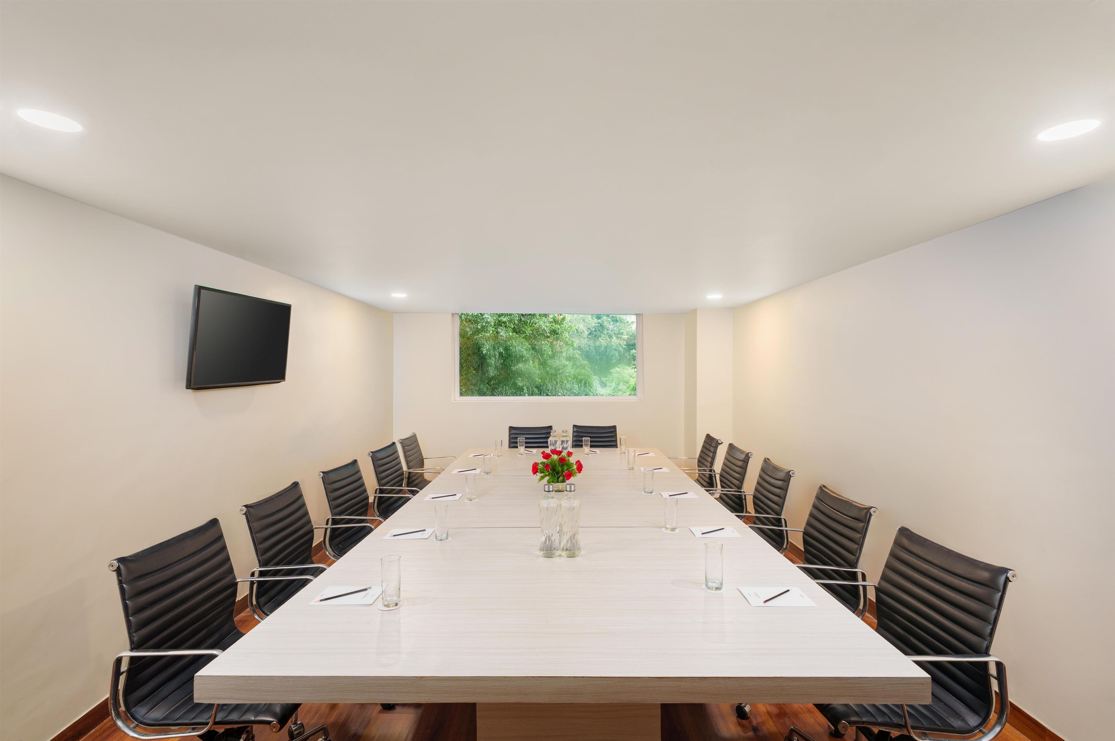 A conference room with a long table, chairs, a TV, and a window with a view of greenery.