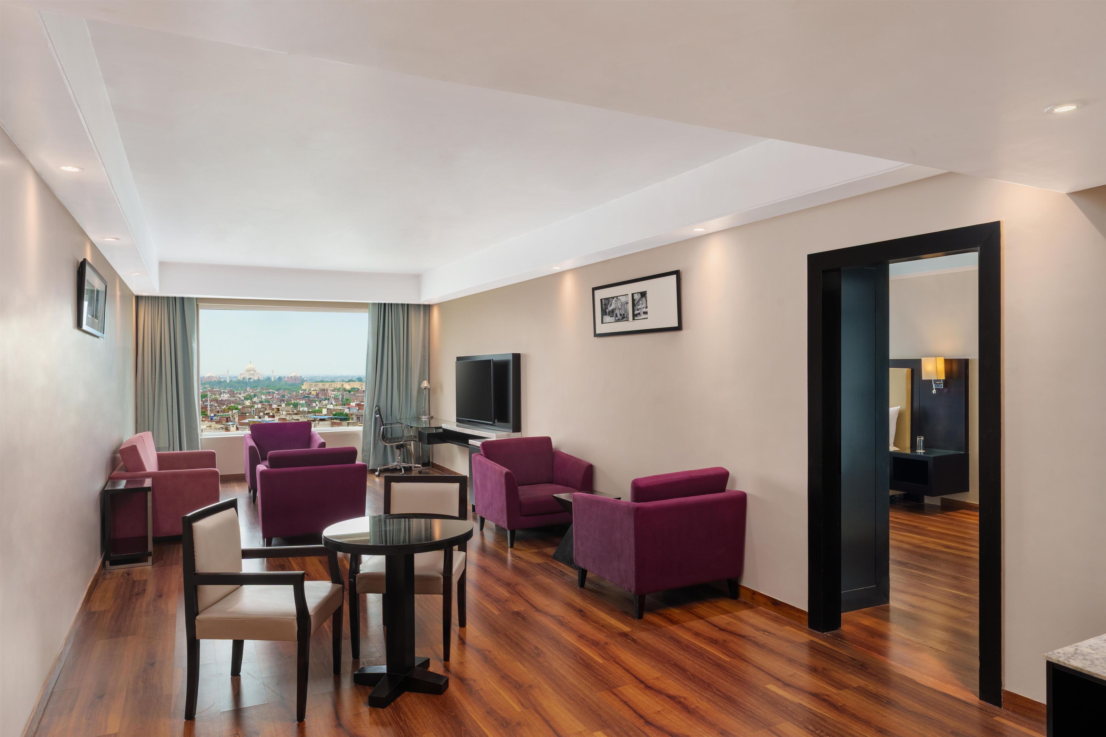 A hotel room with a dining table, purple chairs, a flat-screen TV, and a city view.
