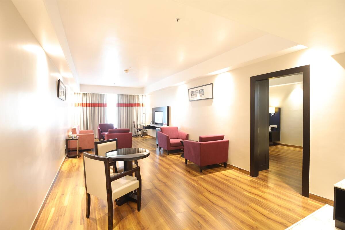 Una habitación de hotel con piso de madera, una mesa de comedor con sillas y varios sofás.