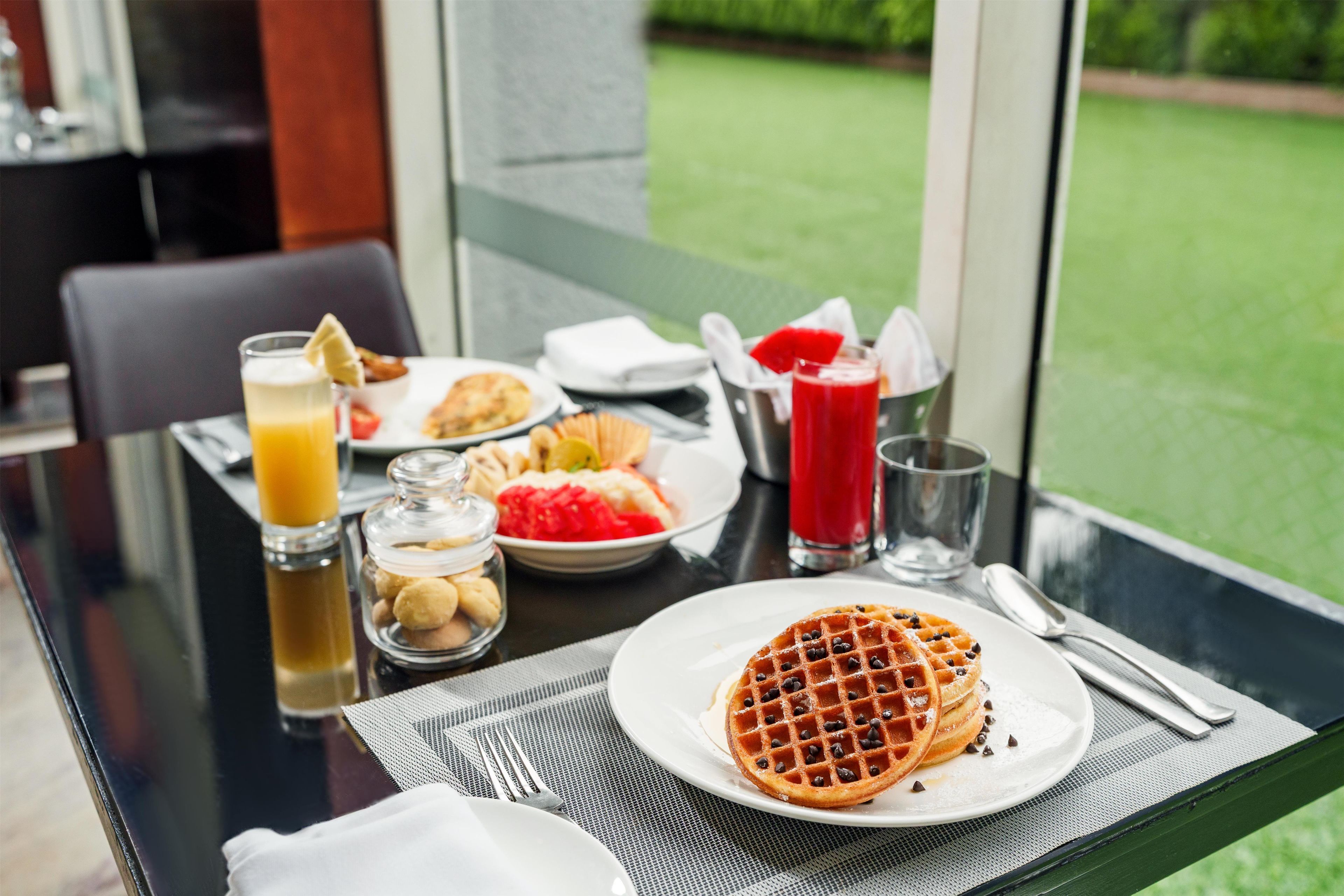 A breakfast table with waffles, a glass of orange juice, and a red drink.