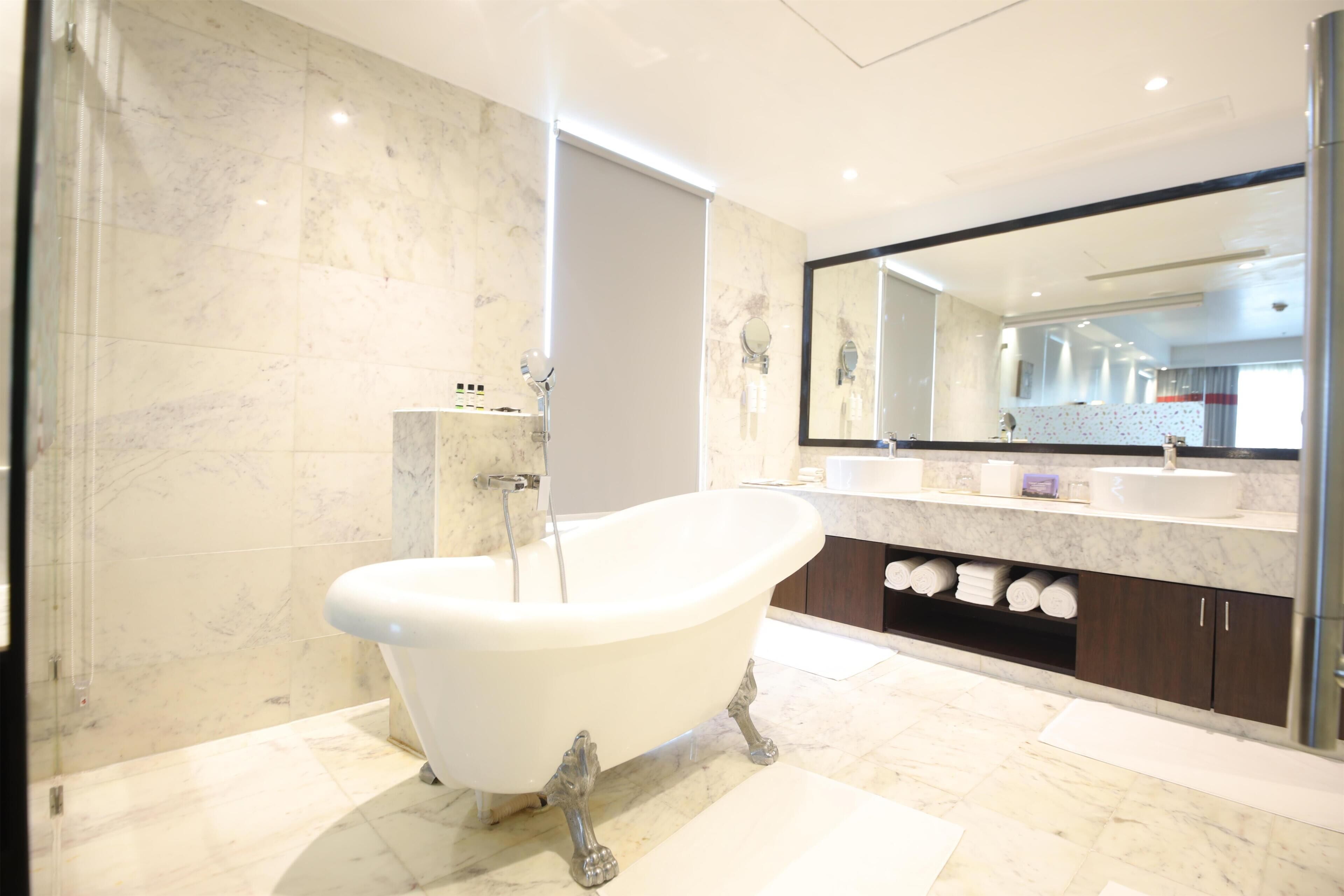 A modern bathroom with a freestanding bathtub, marble walls, a large mirror, and a vanity with a sink.