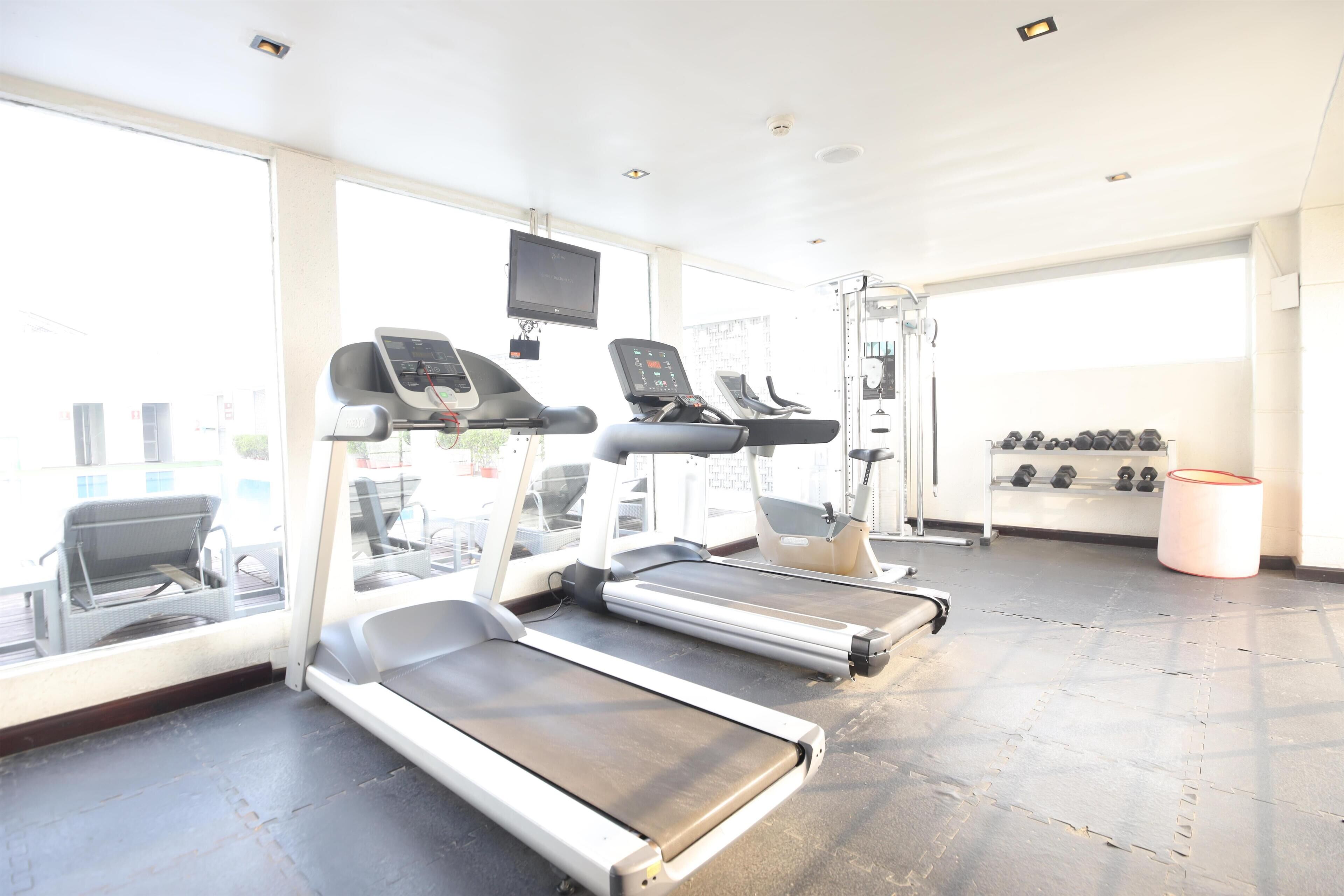 A gym with treadmills, weights, and a TV screen.