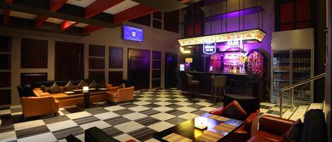 Uma área de bar com piso quadriculado, banquetas e uma tela de televisão.