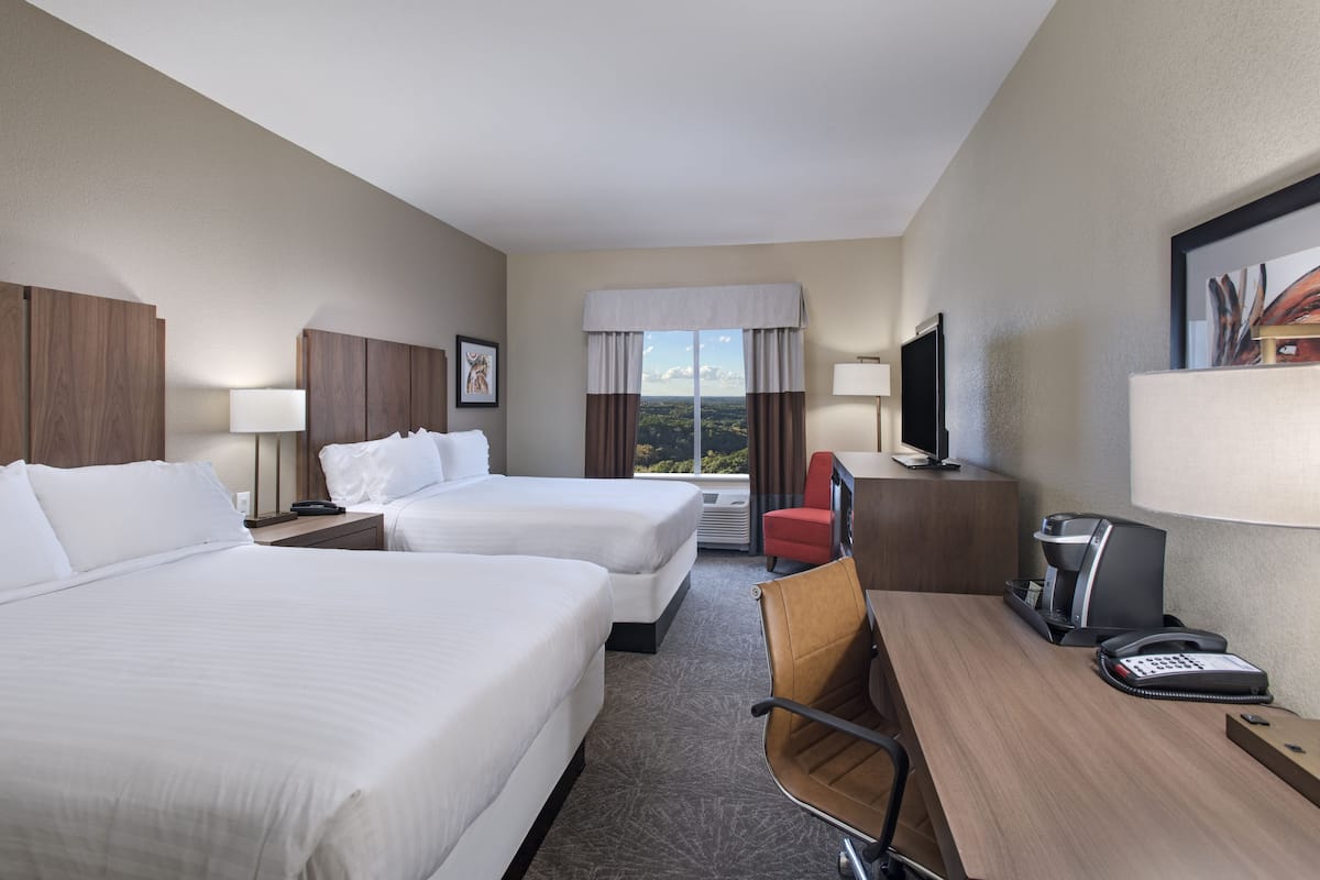 Habitación de hotel con dos camas, un escritorio con silla, televisión y ventana con vistas.