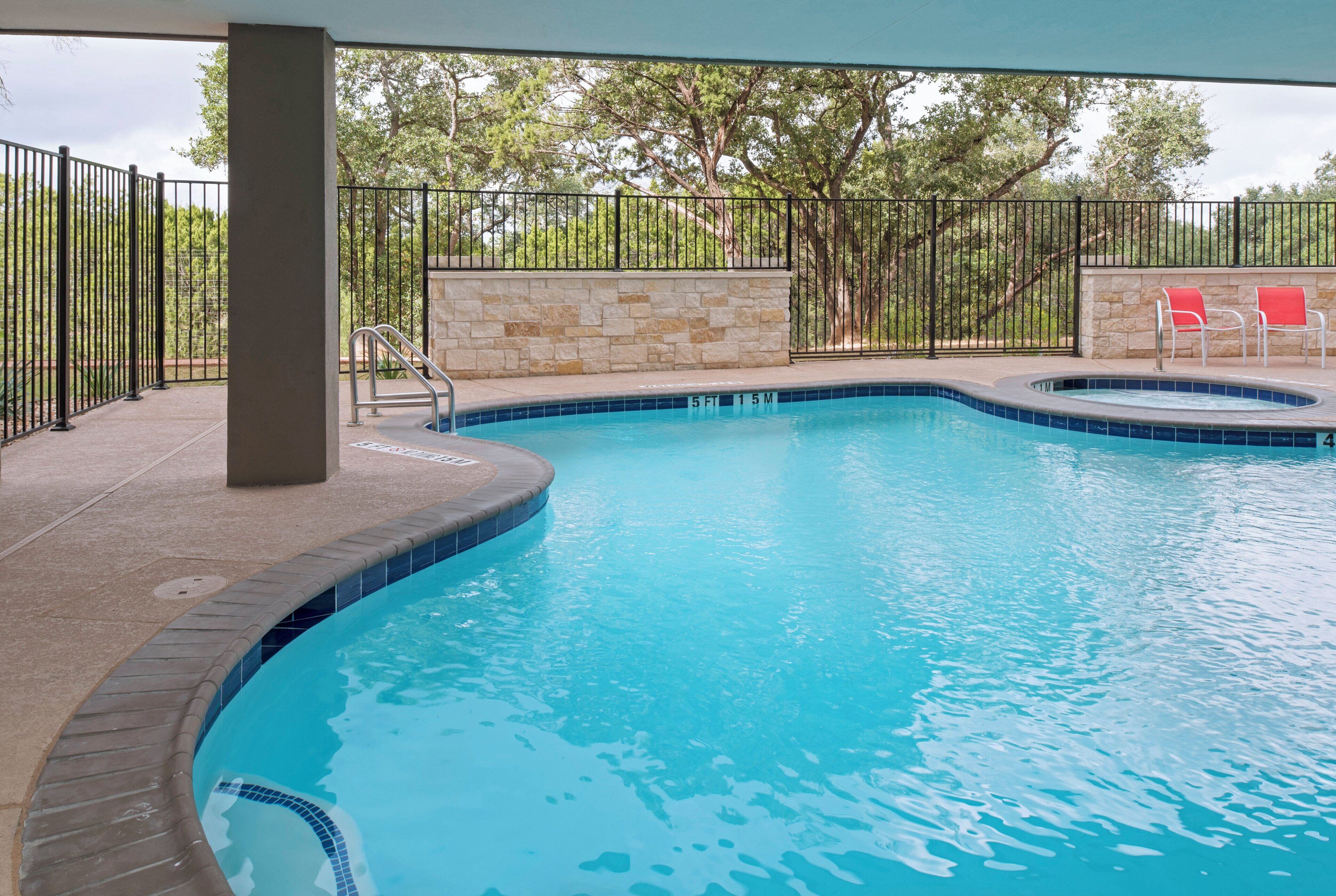 A swimming pool with a stone wall and metal railing, surrounded by trees.