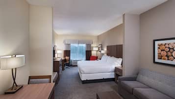 A hotel room with a bed, a desk, a chair, a sofa, and a lamp.