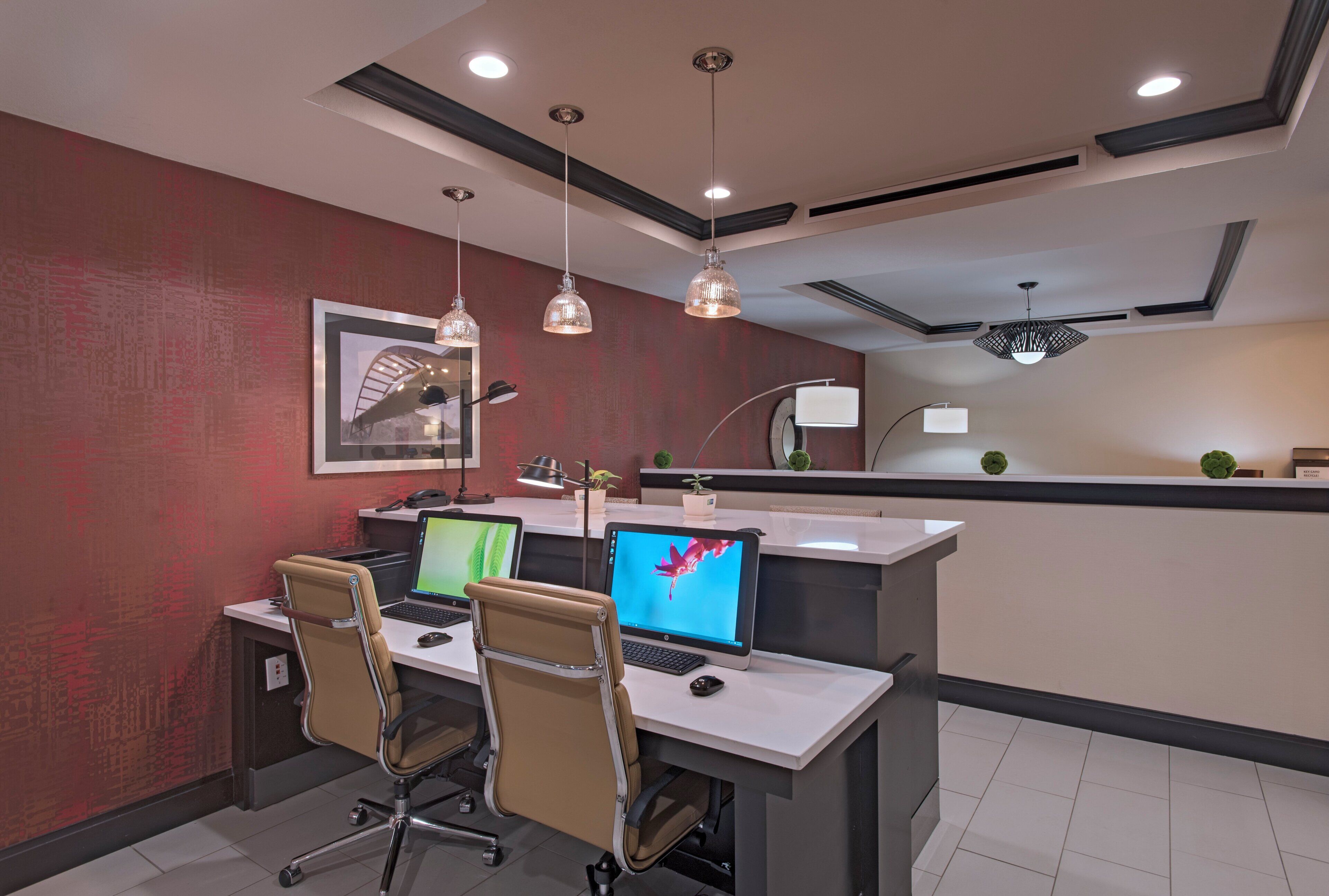 A modern office space with a desk, two chairs, two laptops, and a desktop computer.