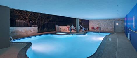 An indoor swimming pool with a stone wall, a metal fence, and chairs.