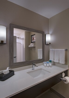 Un bagno d'hotel con uno specchio grande, un lavandino, un porta asciugamani e articoli da toilette.