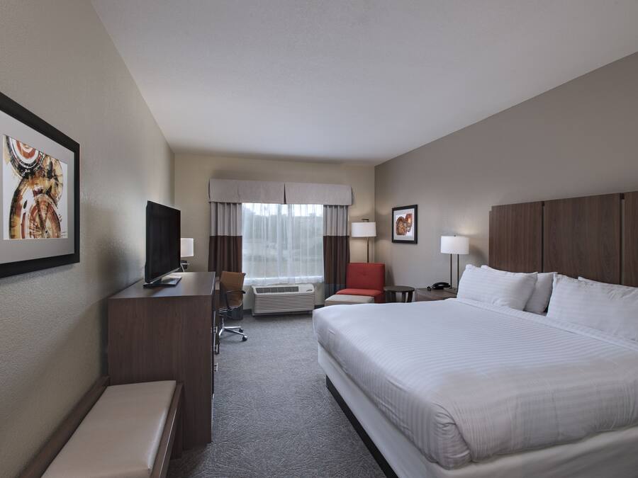 Habitación de hotel con una cama grande, un escritorio con televisor, una silla, una mesita y una ventana con cortinas.