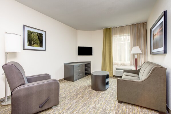 A hotel room with a sofa, a chair, a TV, a lamp, and a picture on the wall. - Candlewood Suites Cut Off by IHG (Cut Off)