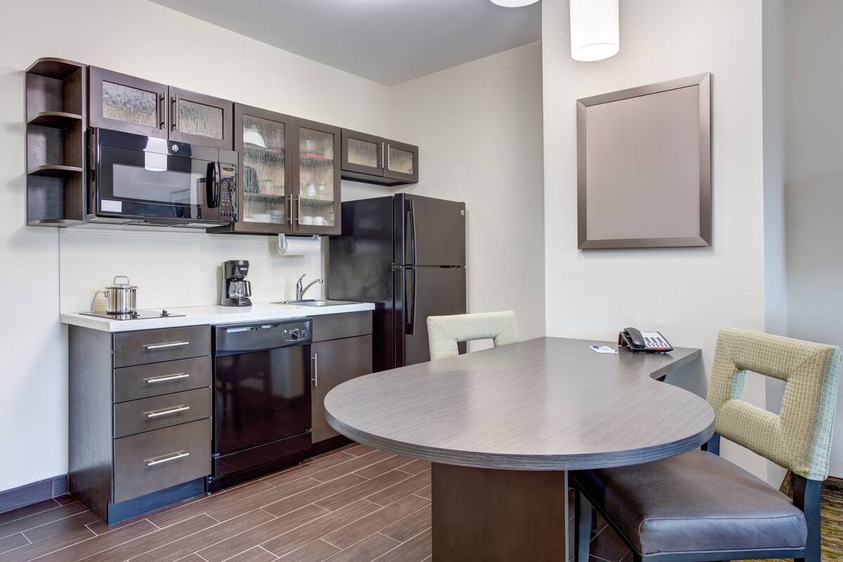 A compact kitchen with a microwave, refrigerator, and dishwasher. There's a dining table with chairs and a phone on the counter.