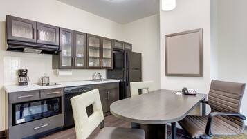 A modern kitchen with dark cabinets, a refrigerator, a coffee maker, and a dining area with a table and chairs.