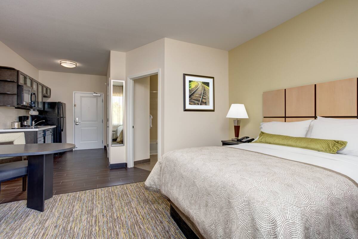 A hotel room with a bed, bedside table, lamp, and a view of the hallway.