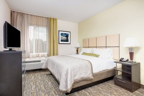 A hotel room with a bed, a desk with a telephone, a television, and a window with curtains. - Candlewood Suites Cut Off by IHG (Cut Off)