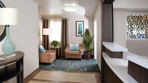 A hotel lobby with a reception desk, a seating area with two sofas, a small table with a lamp, and a large mirror. - Candlewood Suites Cut Off by IHG (Cut Off)