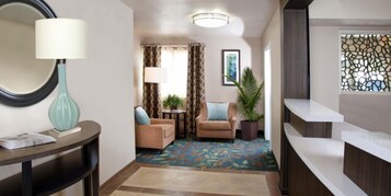 A hotel lobby with a reception desk, a seating area with two sofas, a small table with a lamp, and a large mirror.
