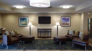 A hotel lobby with a brown leather sofa set, two standing lamps, a flat-screen TV, and framed artwork on the walls. - Candlewood Suites Cut Off by IHG (Cut Off)