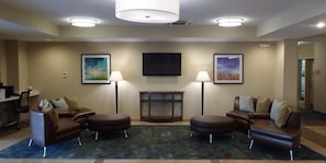 A hotel lobby with a brown leather sofa set, two standing lamps, a flat-screen TV, and framed artwork on the walls. - Candlewood Suites Cut Off by IHG (Cut Off)