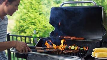 Una persona asando comida en una parrilla al aire libre con un asa metálica y una tapa.