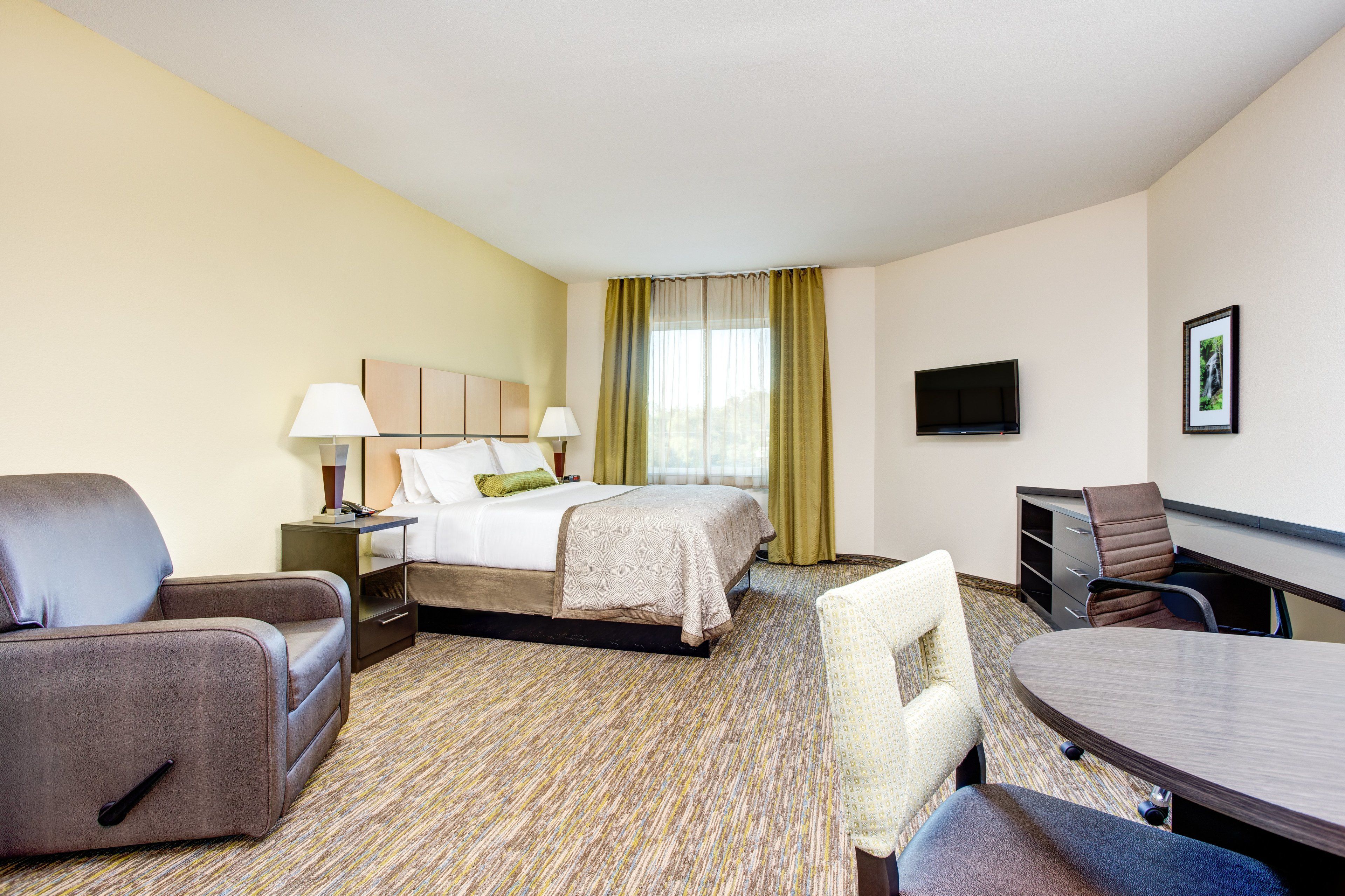A hotel room with a bed, a desk, a chair, a TV, and a lamp.