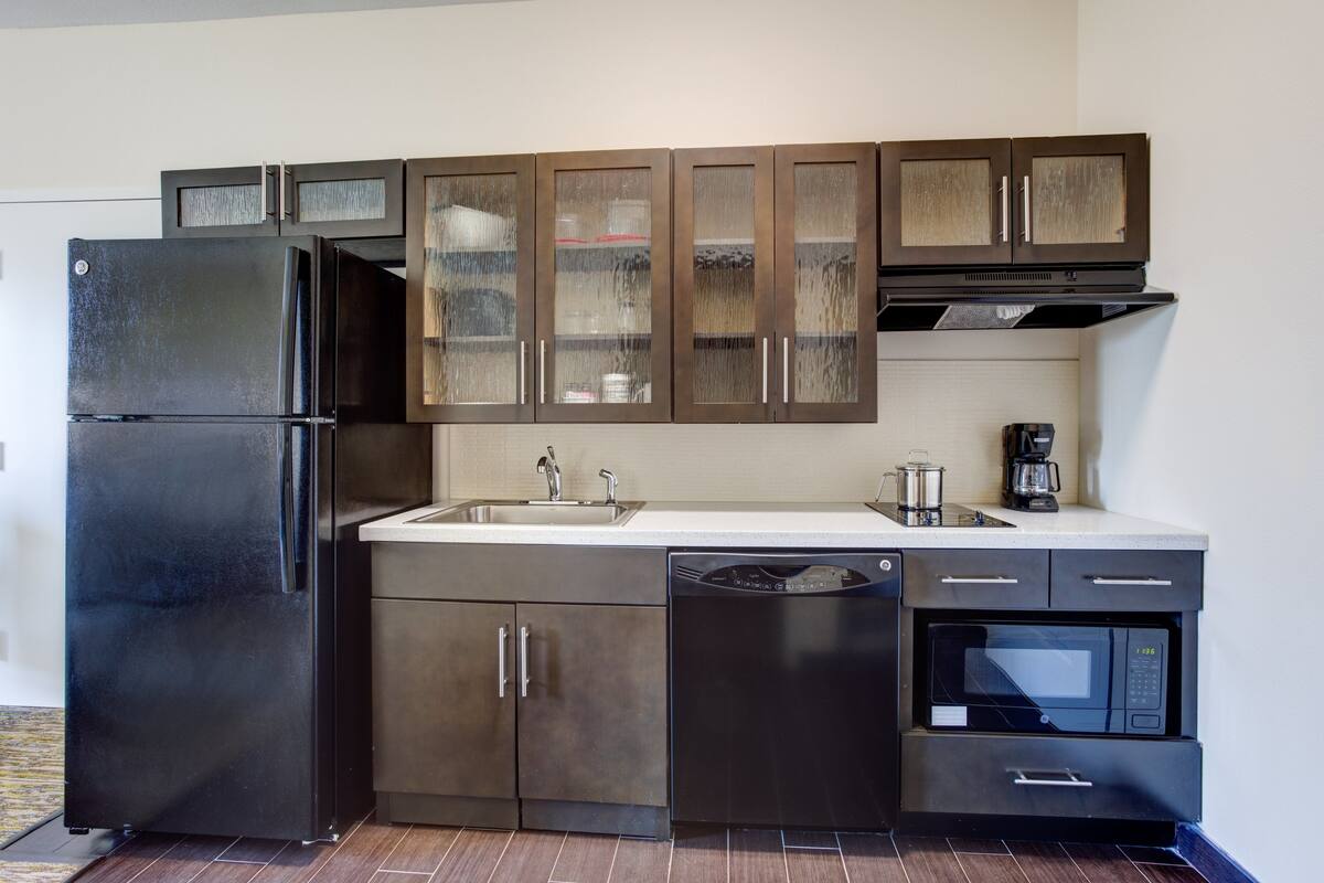 A modern kitchen with a black refrigerator, stainless steel appliances, and wooden cabinets.