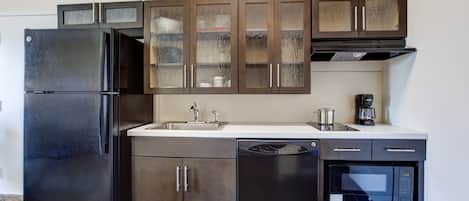 A modern kitchen with a black refrigerator, stainless steel appliances, and wooden cabinets.