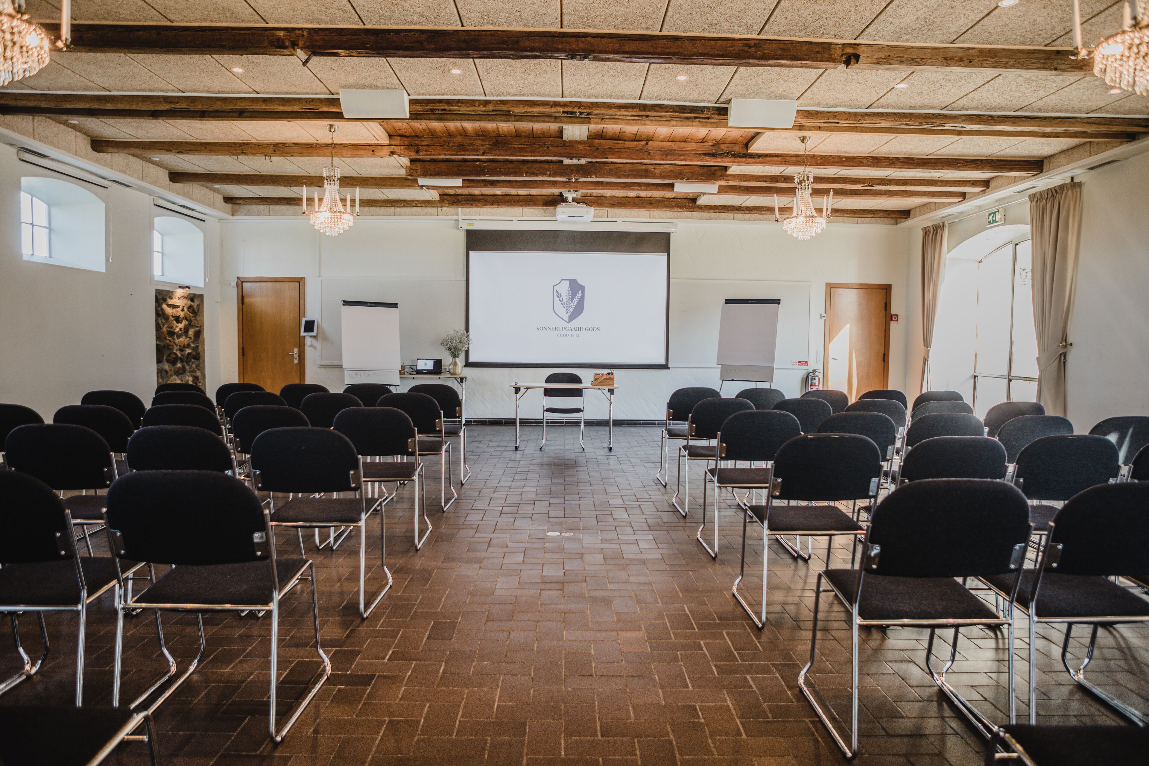 A conference room with rows of chairs, a projector screen, and a wooden ceiling.