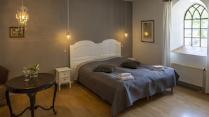 A bedroom with a bed, bedside tables, a small table with a vase, a chandelier, and a window with a view. - Sonnerupgaard Gods (Hvalso)