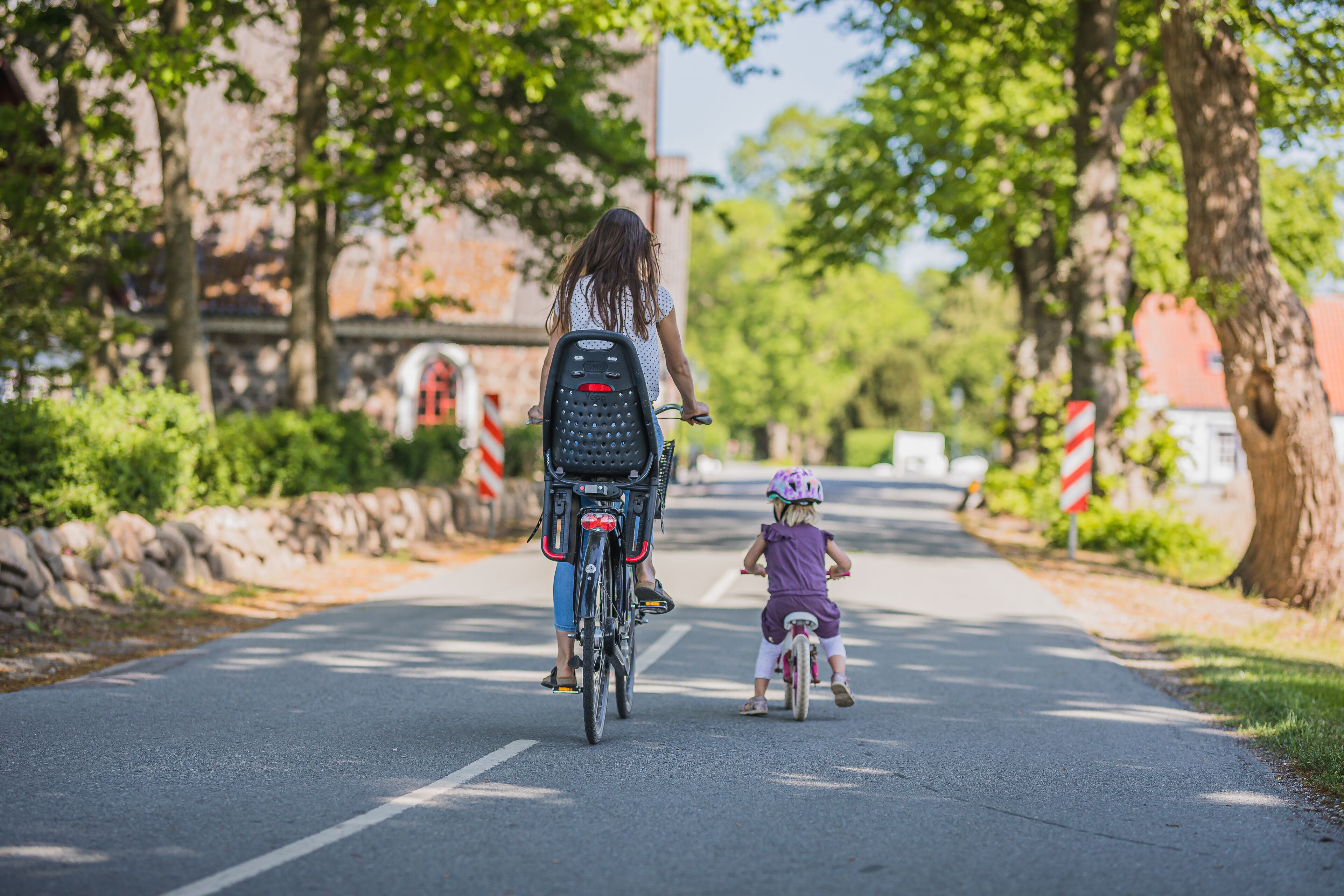 Una donna e un bambino che vanno in bicicletta lungo una strada alberata.