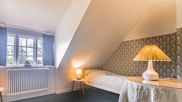 A small, cozy room with a single bed, a table with a lamp, and a radiator.