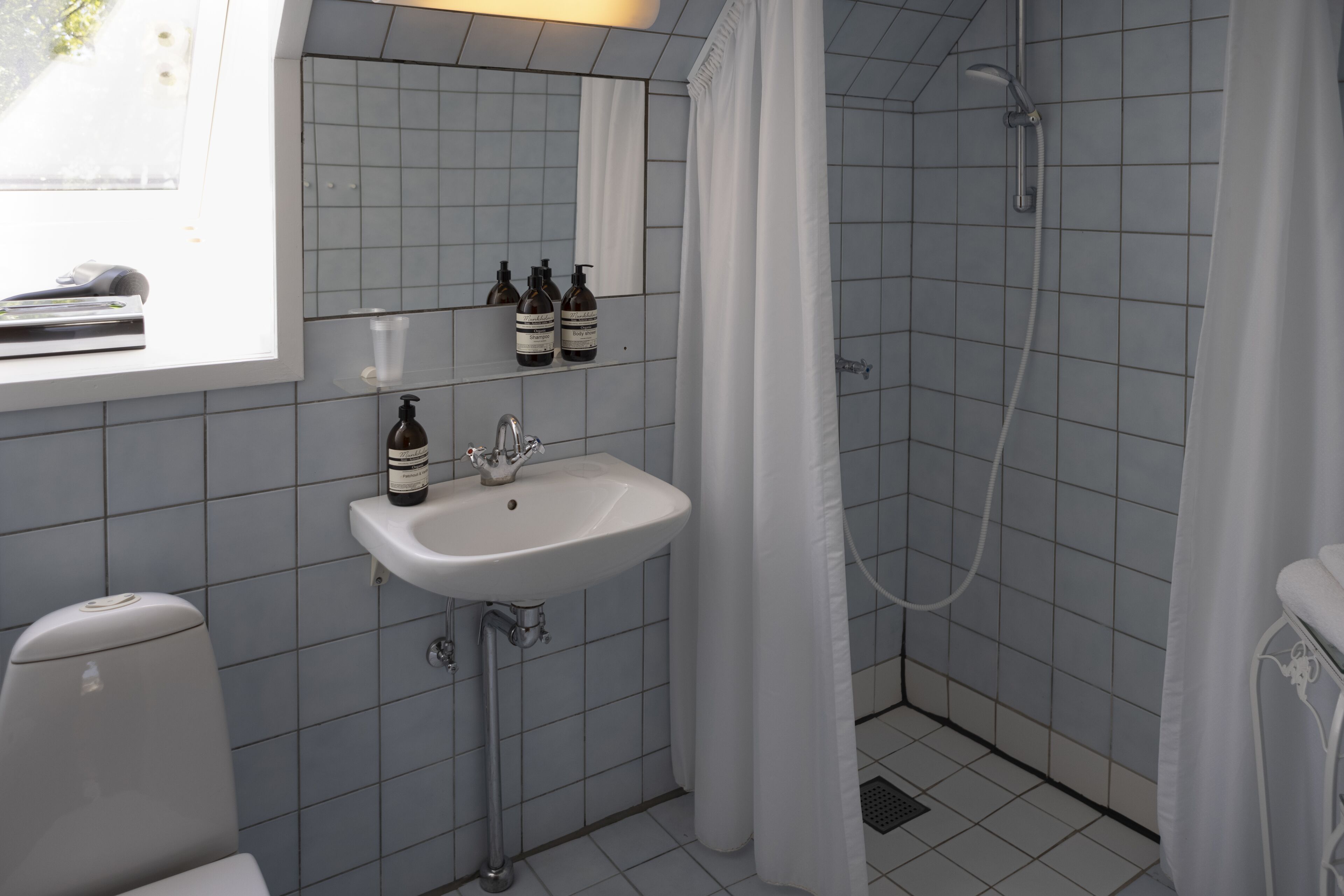 Et badeværelse med vask, spejl og brusebad.