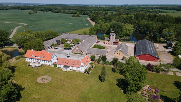 An aerial view of a rural property with a large house, a church, and a pond. - Sonnerupgaard Gods (Hvalso)