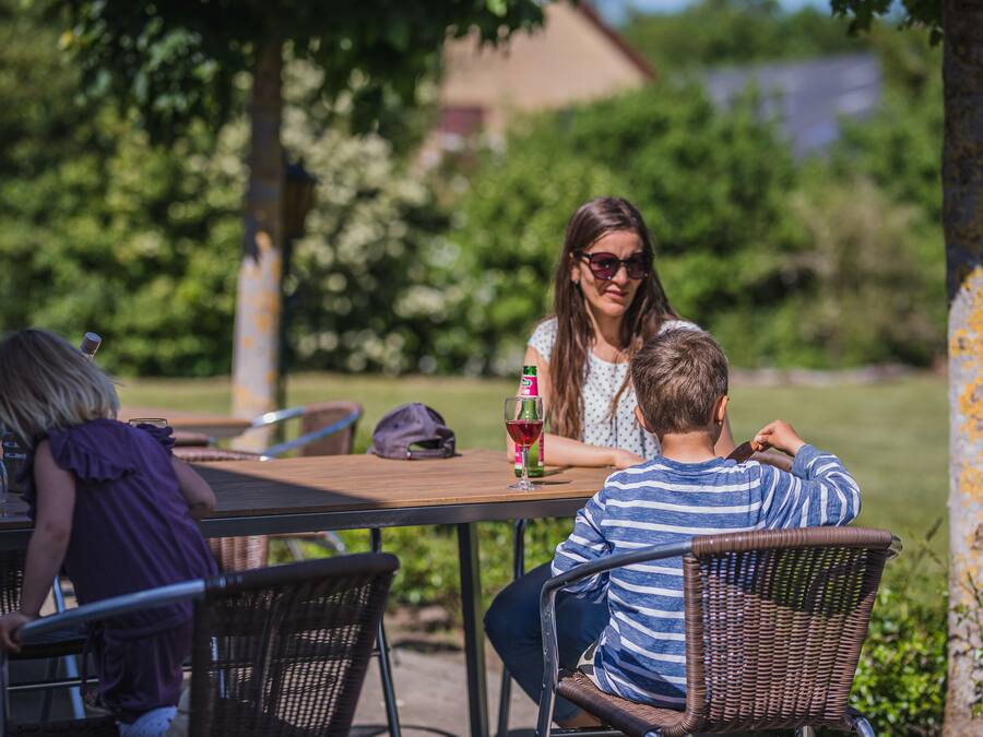 A dining area with outdoor seating, a table with a bottle of wine, and a child playing.