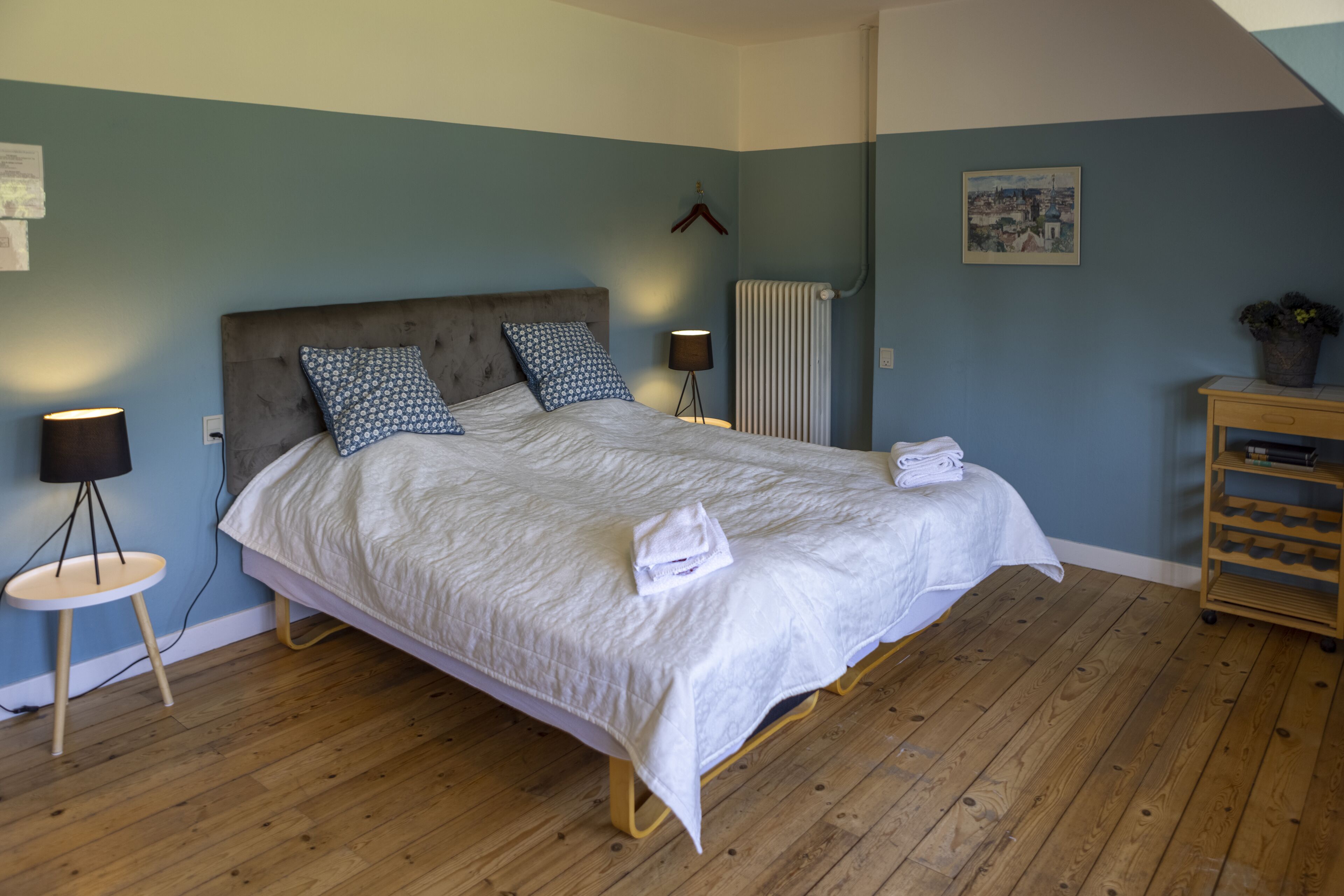 A bedroom with a bed, bedside lamps, a radiator, and a wooden floor.