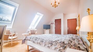 A bedroom with a bed, a desk, a chair, a television, and a chandelier.
